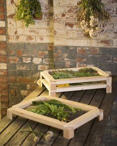 two wooden trays filled with plants sitting on top of a table next to a brick wall