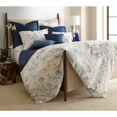 a bed with blue and white comforters in a bedroom next to a lamp on a table