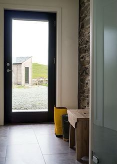 an open door leading to a room with a stone wall and black glass front door