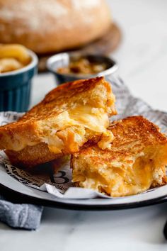 two pieces of grilled cheese sandwich on a plate next to bread bowls and utensils