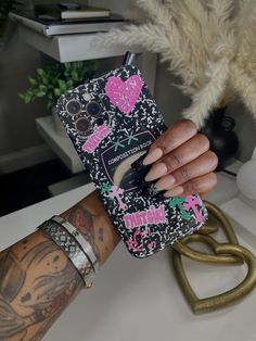 a person holding up a cell phone case with pink and black designs on it's cover