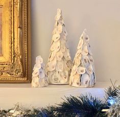 three small christmas trees sitting on top of a mantle covered in seashells and pine cones