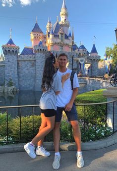 a man and woman standing next to each other in front of a castle at disneyland