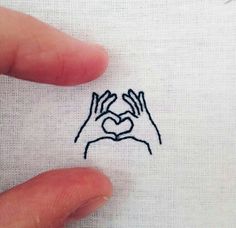 two hands making a heart with their fingers on a piece of paper that has been embroidered onto it