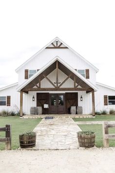 a white barn with two wooden barrels in front of it and an entry way leading into the building