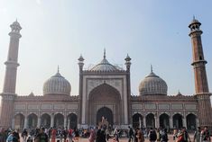 many people are walking around in front of a large building with two tall towers on each side