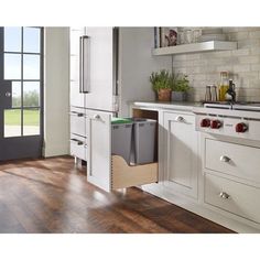 a kitchen with white cabinets and wood flooring has an open trash can in the middle