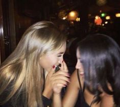 two beautiful young women sitting next to each other in front of a bar talking on their cell phones