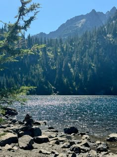 a lake surrounded by rocks and trees with mountains in the background