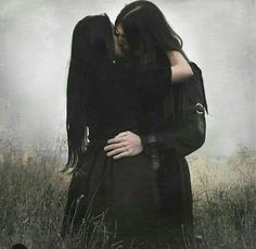 two people standing in the grass with their arms around each other and one person kissing