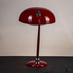 a red table lamp sitting on top of a black floor next to a white wall