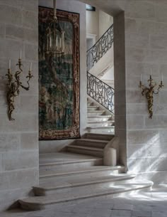 an ornate staircase with chandelier and tapestry hanging on the wall in front of it