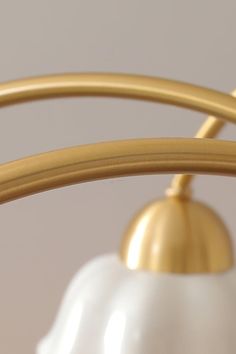 a white and gold tea pot is hanging from a brass ring on the ceiling light