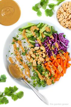 a white plate topped with rice, carrots and veggies next to peanut sauce