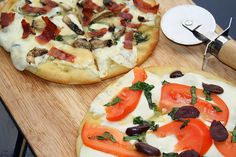 two pizzas sitting on top of a wooden cutting board