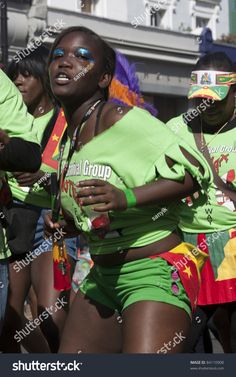 a group of women in green shirts and shorts dancing on the street with other people behind them