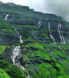 a lush green hillside covered in lots of tall waterfall cascading next to a road