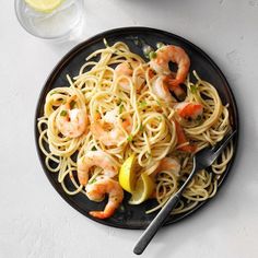 a plate of pasta with shrimp and lemon wedges