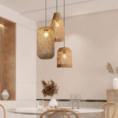 three lights hanging from the ceiling above a table with chairs and vases on it