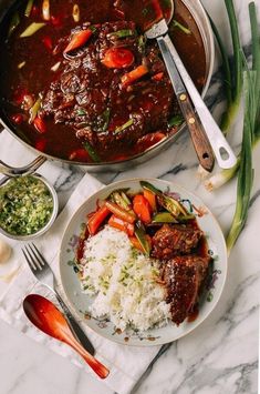 a plate with rice, meat and vegetables on it next to a pot of stew