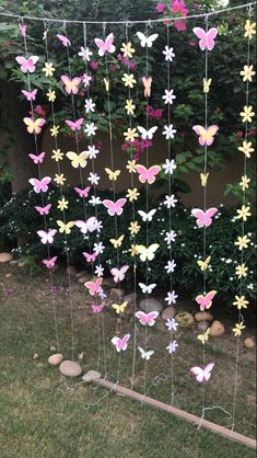 some paper butterflies hanging from a wire in front of a bush with rocks and grass