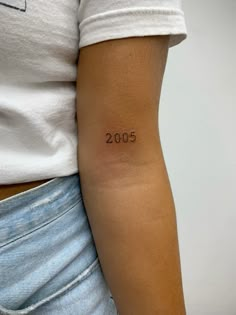 a woman with a small tattoo on her arm that reads 2050 in cursive writing