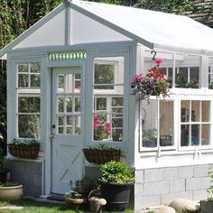 a small white greenhouse with potted plants and flowers in the window boxes on the side