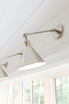 two light fixtures on the ceiling in a room with large windows and white brick walls