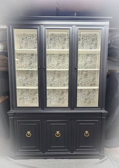 a black china cabinet with glass doors and gold hardware on the bottom, in front of other furniture