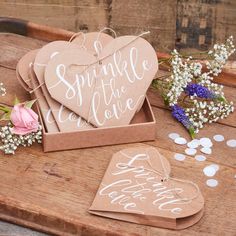 two heart shaped tags sitting on top of a wooden table next to flowers and confetti