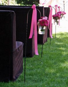 rows of black and pink flower arrangements in vases with ribbons tied to them on the grass