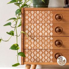 a wooden dresser with three drawers and two plants on top of it next to a potted plant