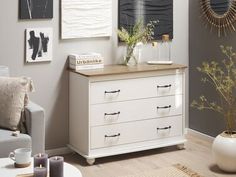 a white dresser sitting in a living room next to a gray wall with pictures on it