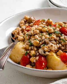 a white bowl filled with rice and vegetables next to a fork on a tablecloth