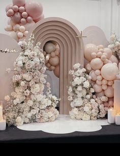 a table topped with lots of white flowers and balloons in front of a wall filled with balloons