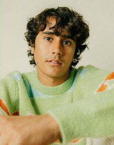 a young man with curly hair wearing a green sweater and pointing to the left side