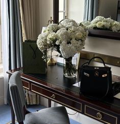 a desk with flowers and a handbag on it in front of a large mirror