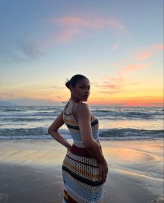 a woman standing on top of a beach next to the ocean in front of a sunset