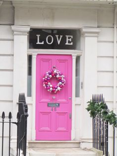 a pink front door with a wreath on it and the words love above it is in black lettering