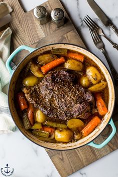 a pot filled with meat and vegetables on top of a wooden table next to utensils