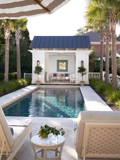 an outdoor pool with lounge chairs and tables next to it, surrounded by palm trees