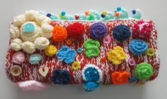 a red and white knitted purse with crochet flowers on the front, buttons in the back