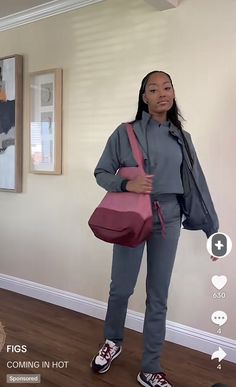 a woman holding a pink handbag standing in front of a wall with pictures on it