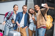 four people taking a selfie while standing in front of a camper with their luggage