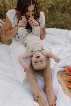 a woman holding a baby laying on top of a bed next to watermelon