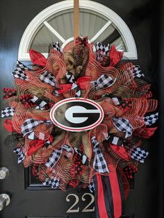 a wreath with the letter g on it is hanging on a black door and has red, white, and black checkered ribbon