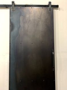 a black metal door with rivets on the bottom and sides, hanging from a white wall