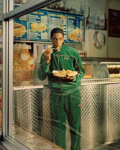 a man standing in front of a fast food restaurant holding a plate of food and looking at the camera