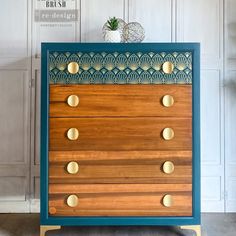 a blue and wooden dresser with brass knobs on it's sides, against a white wall