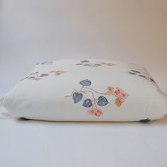 a white pillow with blue and pink flowers on it sitting on top of a table